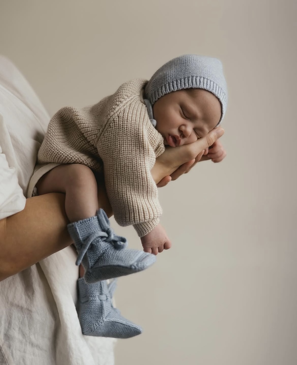Baby in gebreide trui, muts en slofjes, slaperig in iemands armen