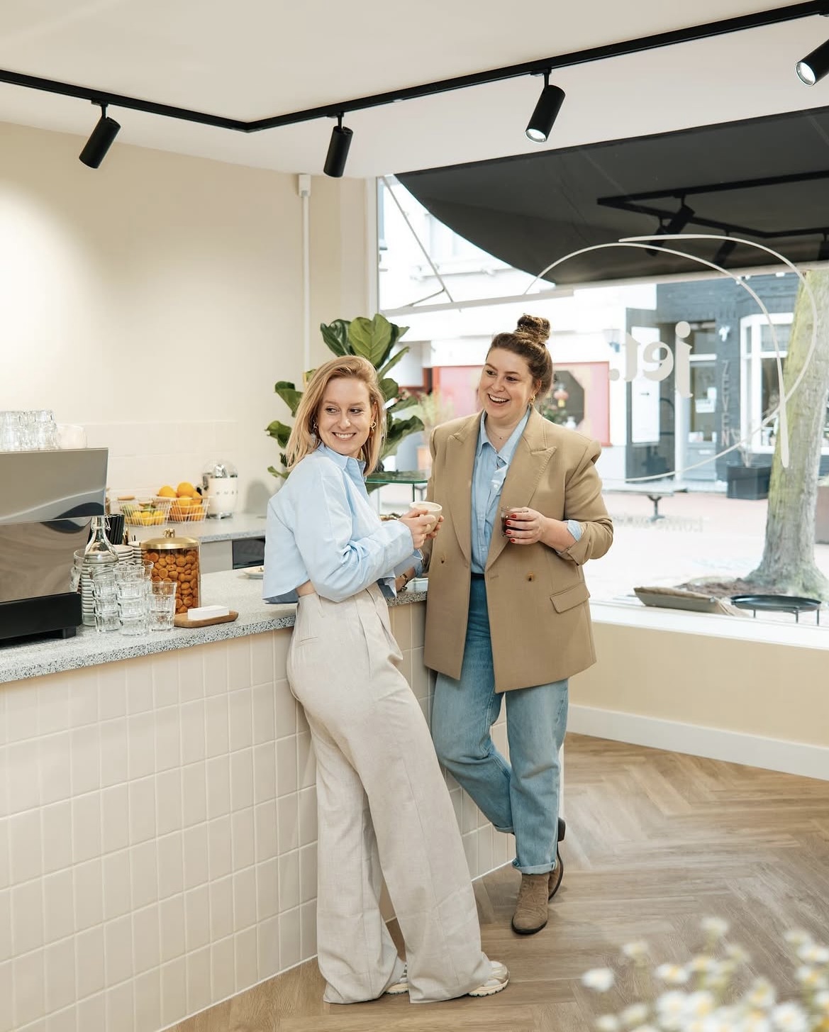 Jet en haar zus lachend aan de bar, met de winkelruit op de achtergrond