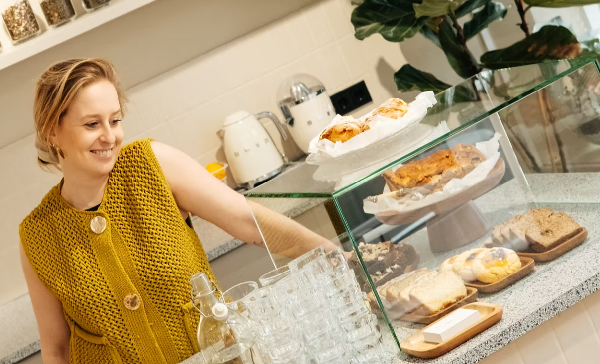 Jet achter de bar, lachend bij de vitrine met vers gebak